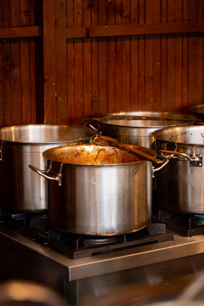 Stainless steel cooking pots with wooden spatula on a stove in a restaurant kitchen.