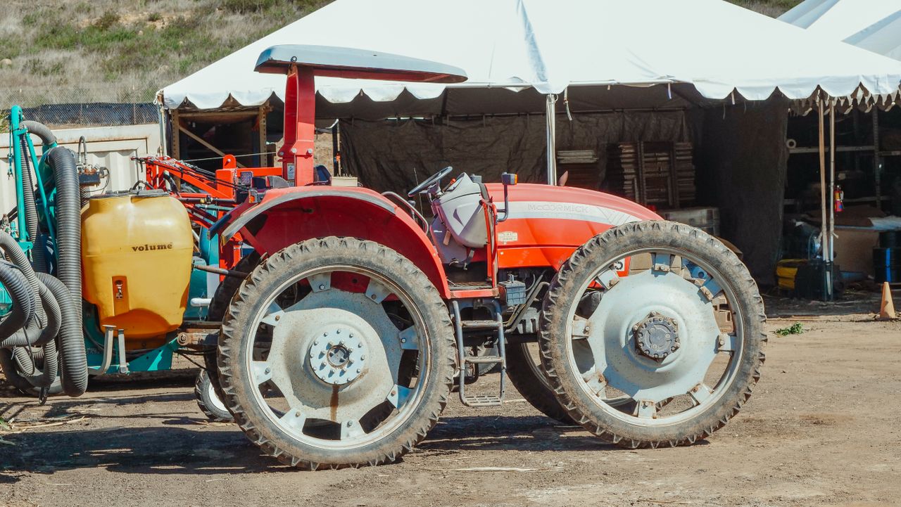 Close-up of a red tractor parked outdoors beside a tent on a farm.