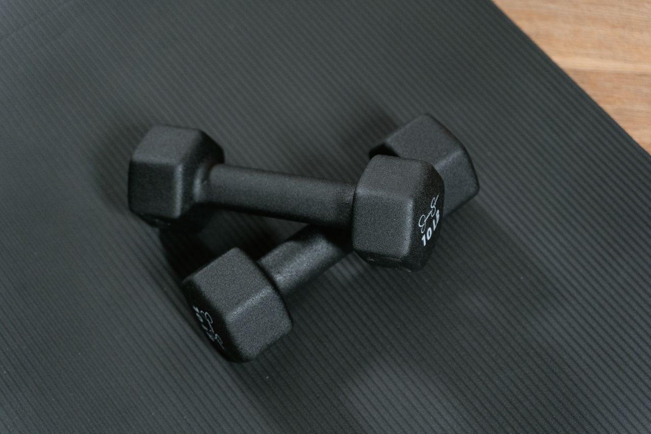 services-01 Black dumbbells placed on a yoga mat, perfect for home workouts and strength training.
